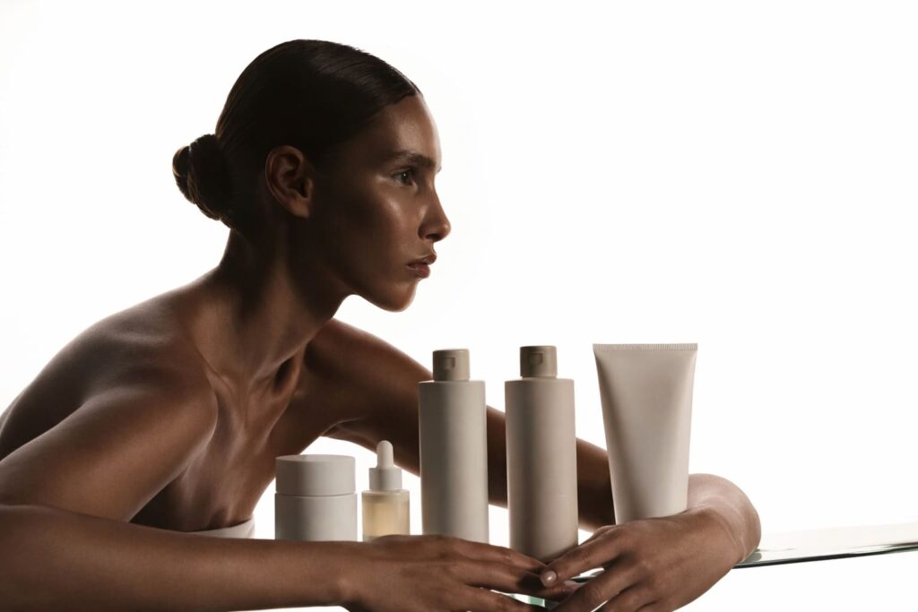 Wide editorial beauty portrait of a woman beside unbranded skincare products, styled with soft neutral tones and the refined quiet luxury aesthetic of NOUA Studio.